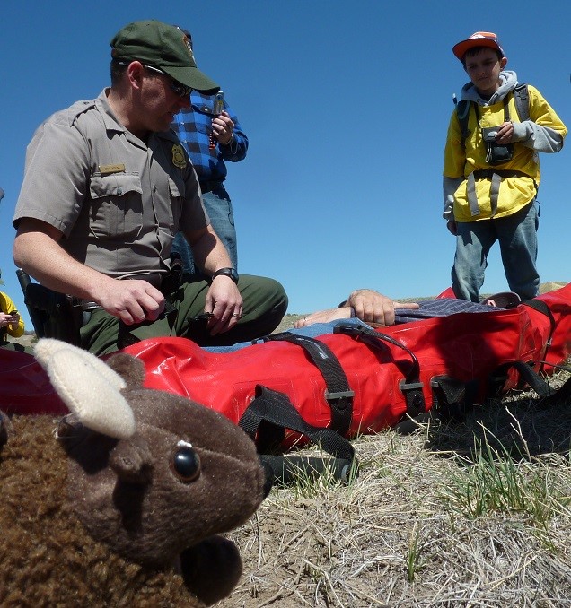 美國惡地國家公園解說員Eric Yount 正向學生展示野地急救方法，右下方為吉祥物野牛兄弟娃娃